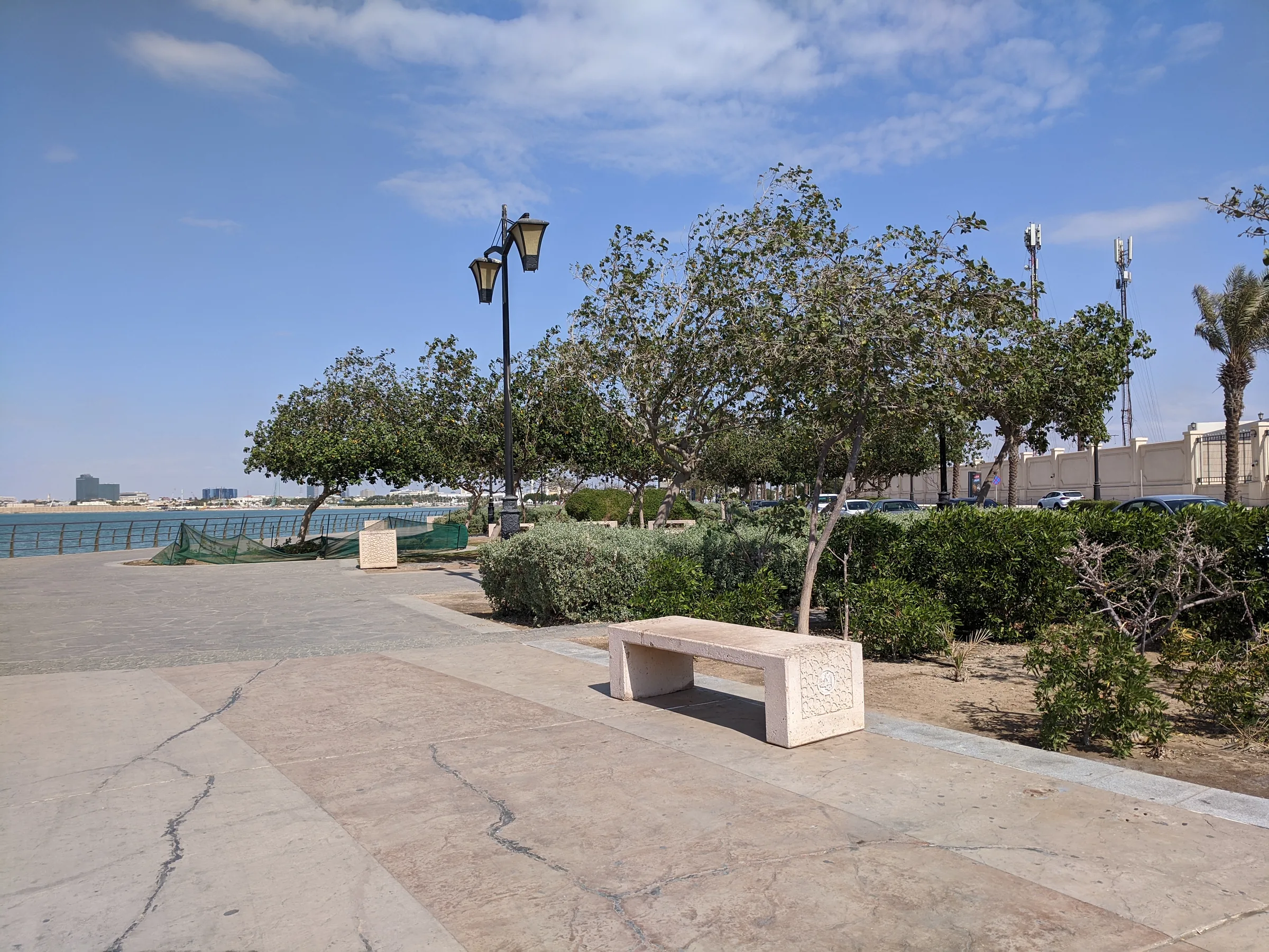 Paved promenade with a stone bench and trees along the Jeddah Corniche waterfront