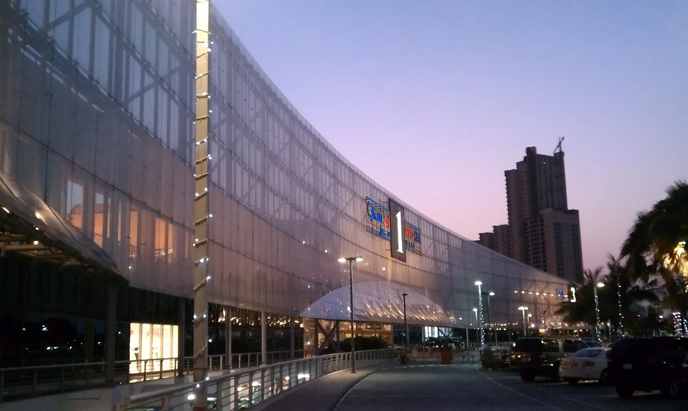 Red Sea Mall's curved glass facade lit up at dusk